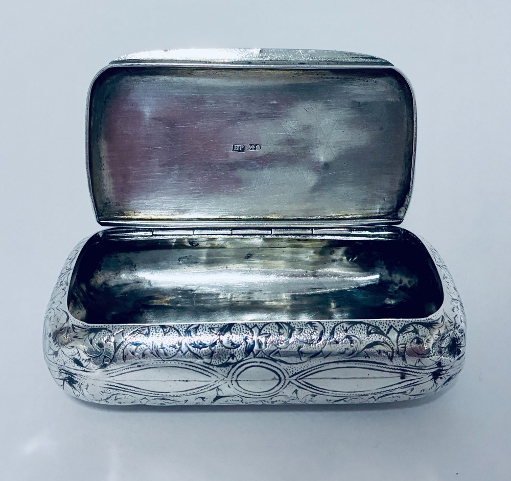 A small, rectangular silver snuff box with rounded corners featuring intricate hand-engraved scrollwork patterns and a central oval cartouche. View III