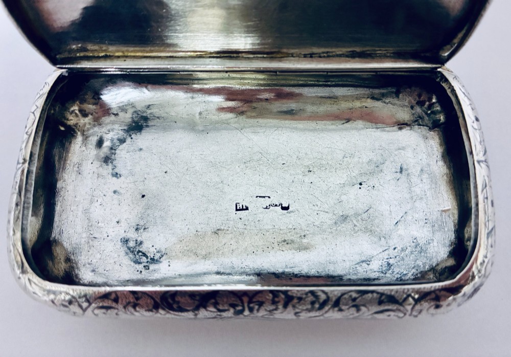 A small, rectangular silver snuff box with rounded corners featuring intricate hand-engraved scrollwork patterns and a central oval cartouche. View V