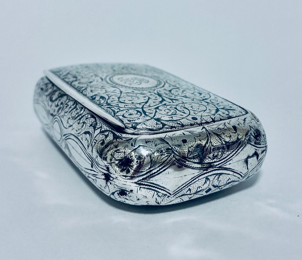 A small, rectangular silver snuff box with rounded corners featuring intricate hand-engraved scrollwork patterns and a central oval cartouche. View VI