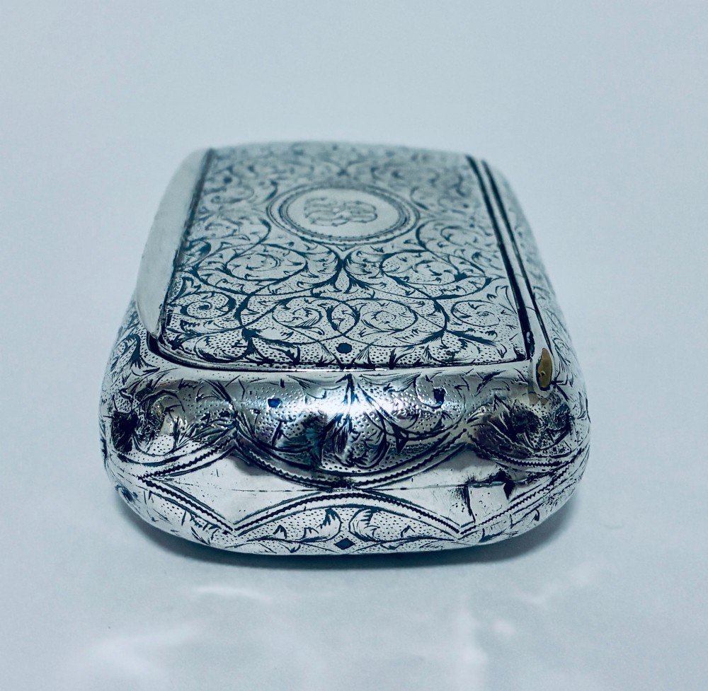 A small, rectangular silver snuff box with rounded corners featuring intricate hand-engraved scrollwork patterns and a central oval cartouche. View VII