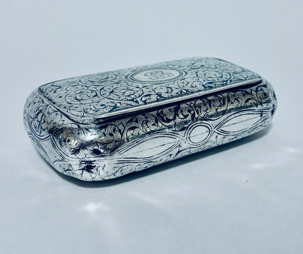 A small, rectangular silver snuff box with rounded corners featuring intricate hand-engraved scrollwork patterns and a central oval cartouche. View X