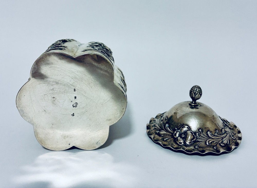 A lobed silver tea caddy with embossed floral patterns, a wavy rimmed lid, and a pinecone-shaped finial. View VII