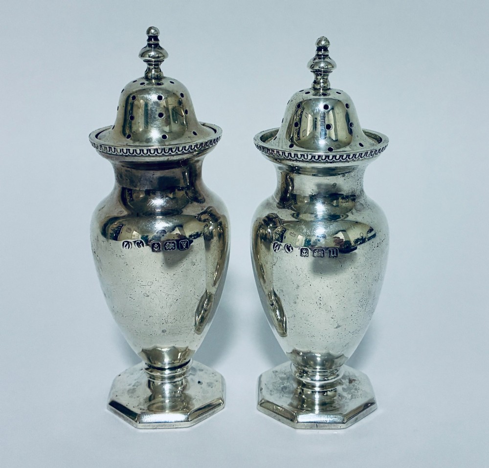 A pair of hallmarked sterling silver baluster pepper pots featuring pierced domed lids with finials and octagonal pedestal bases.