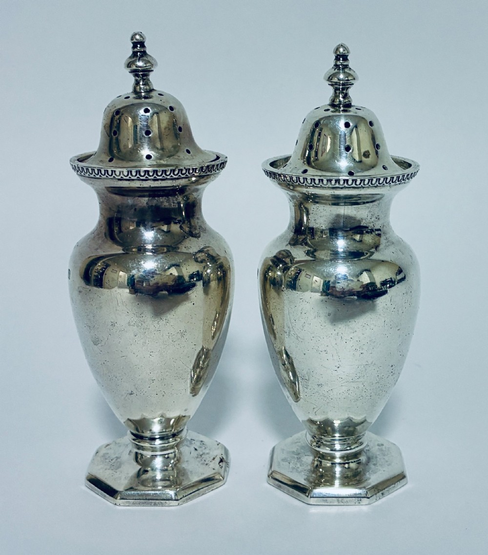 A pair of hallmarked sterling silver baluster pepper pots featuring pierced domed lids with finials and octagonal pedestal bases. View IV