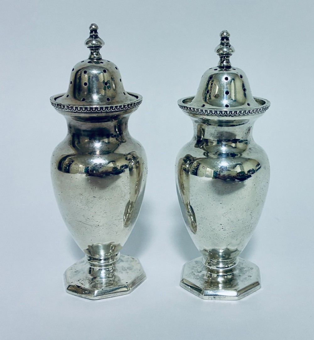 A pair of hallmarked sterling silver baluster pepper pots featuring pierced domed lids with finials and octagonal pedestal bases. View V