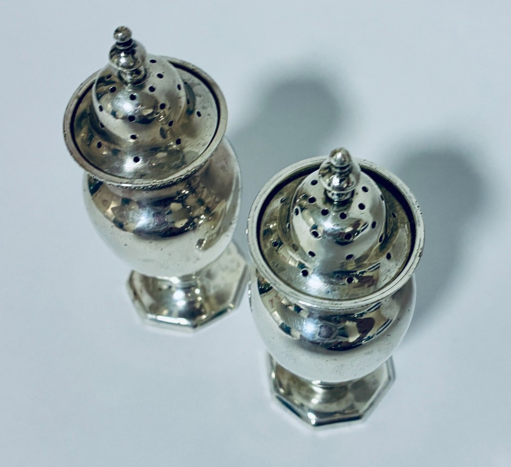 A pair of hallmarked sterling silver baluster pepper pots featuring pierced domed lids with finials and octagonal pedestal bases. View VI