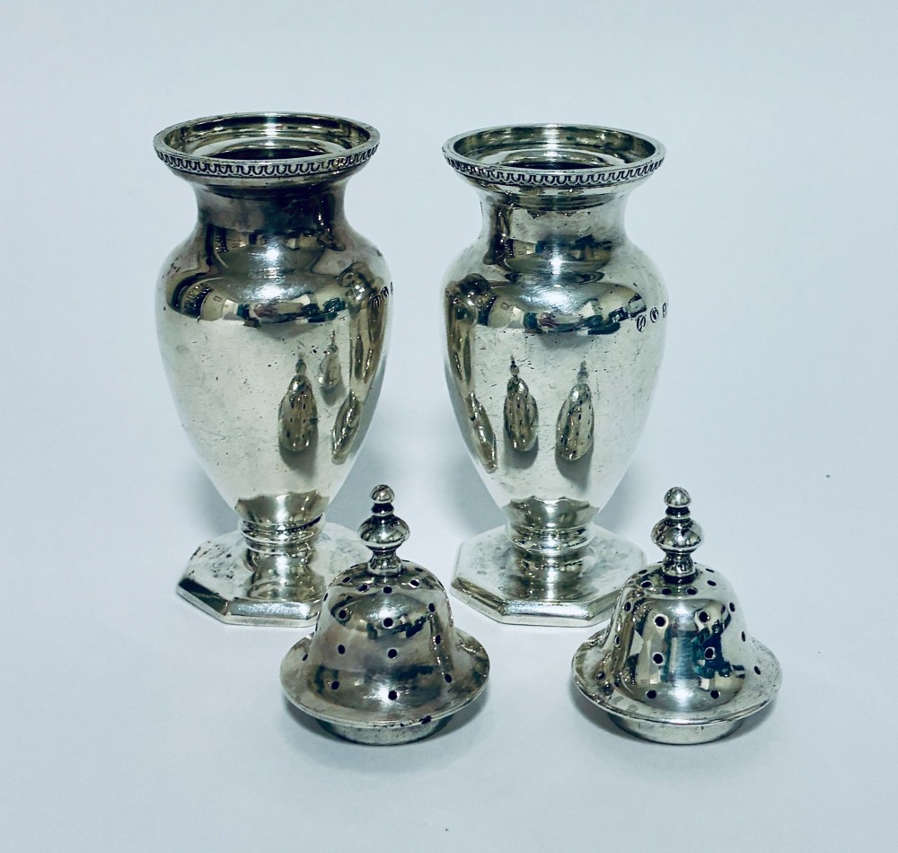 A pair of hallmarked sterling silver baluster pepper pots featuring pierced domed lids with finials and octagonal pedestal bases. View VIII