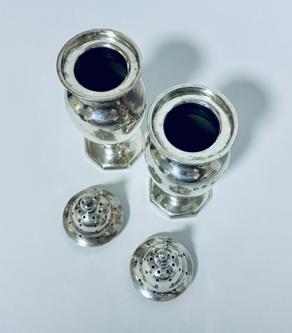 A pair of hallmarked sterling silver baluster pepper pots featuring pierced domed lids with finials and octagonal pedestal bases. View IX