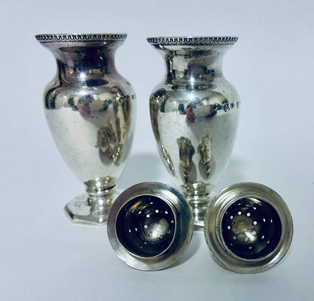 A pair of hallmarked sterling silver baluster pepper pots featuring pierced domed lids with finials and octagonal pedestal bases. View X