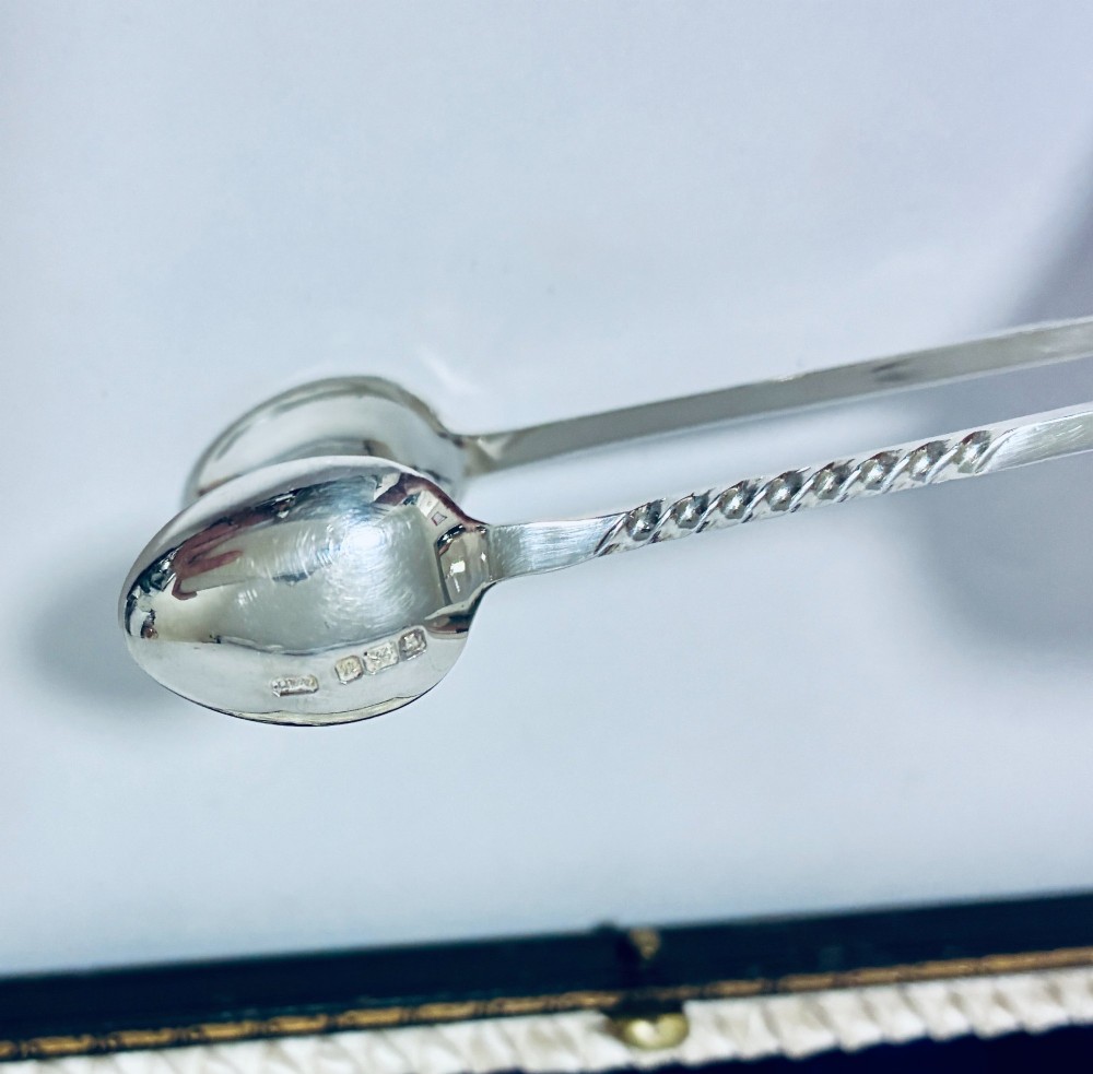 An open dark fitted presentation case lined with white satin and blue velvet containing six silver apostle teaspoons with twisted stems and matching silver sugar tongs. View VI