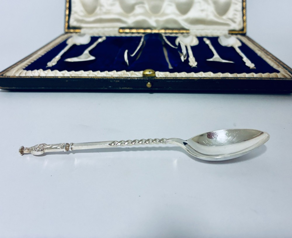 An open dark fitted presentation case lined with white satin and blue velvet containing six silver apostle teaspoons with twisted stems and matching silver sugar tongs. View VII