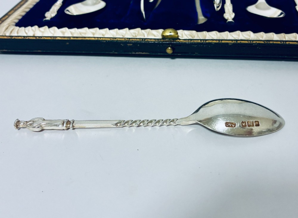 An open dark fitted presentation case lined with white satin and blue velvet containing six silver apostle teaspoons with twisted stems and matching silver sugar tongs. View VIII