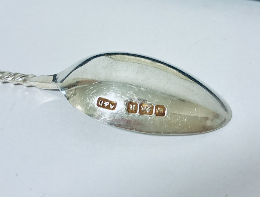 An open dark fitted presentation case lined with white satin and blue velvet containing six silver apostle teaspoons with twisted stems and matching silver sugar tongs. View IX