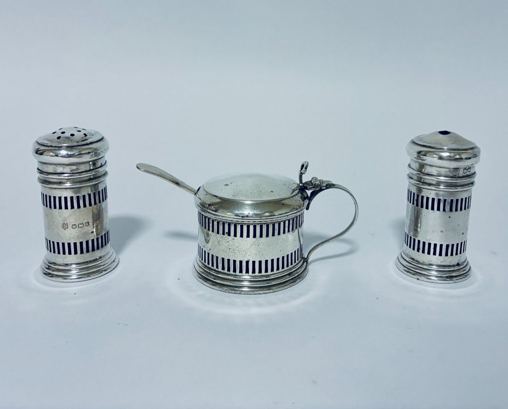 An antique three-piece silver cruet set featuring pierced vertical slot details, a mustard pot with lid and spoon, and two matching pepper casters. View II