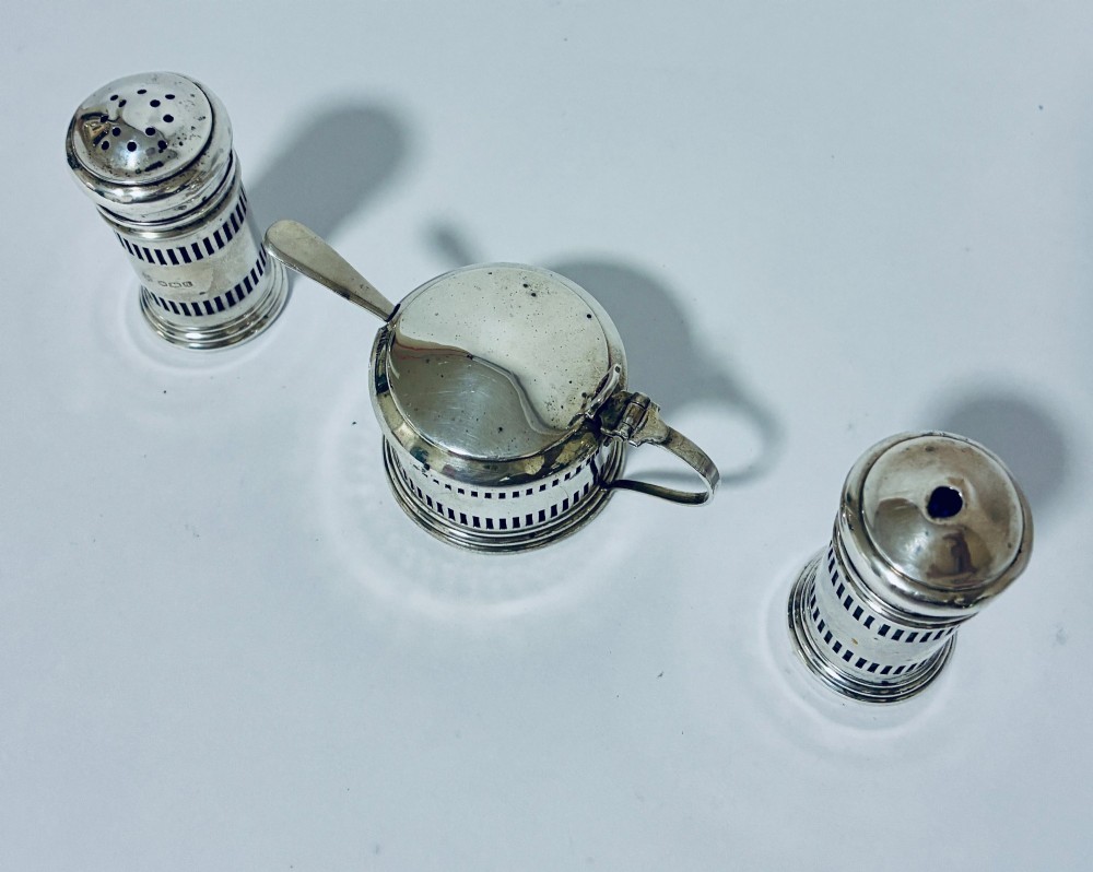 An antique three-piece silver cruet set featuring pierced vertical slot details, a mustard pot with lid and spoon, and two matching pepper casters. View III