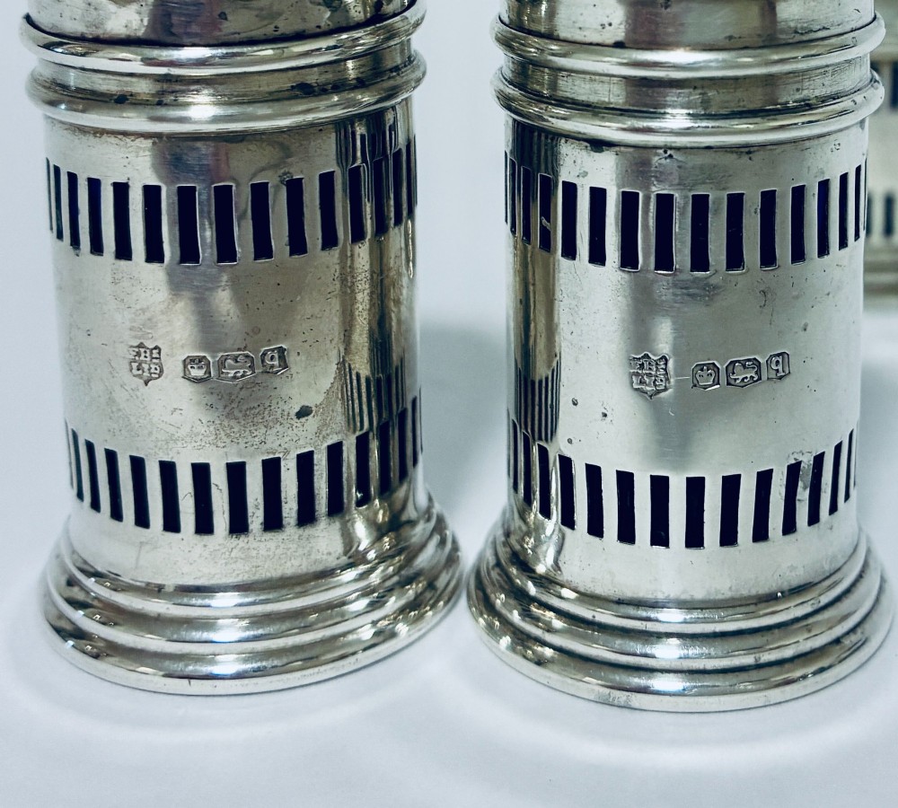 An antique three-piece silver cruet set featuring pierced vertical slot details, a mustard pot with lid and spoon, and two matching pepper casters. View IV