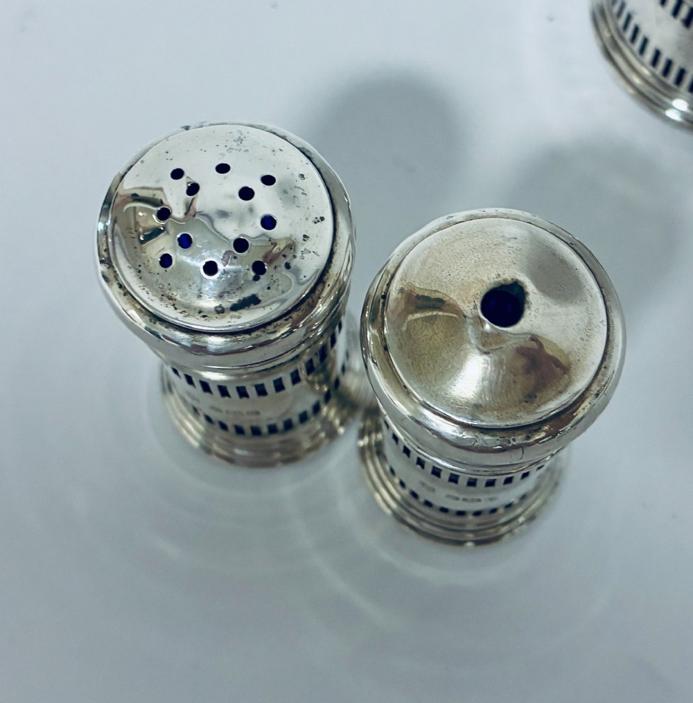 An antique three-piece silver cruet set featuring pierced vertical slot details, a mustard pot with lid and spoon, and two matching pepper casters. View V
