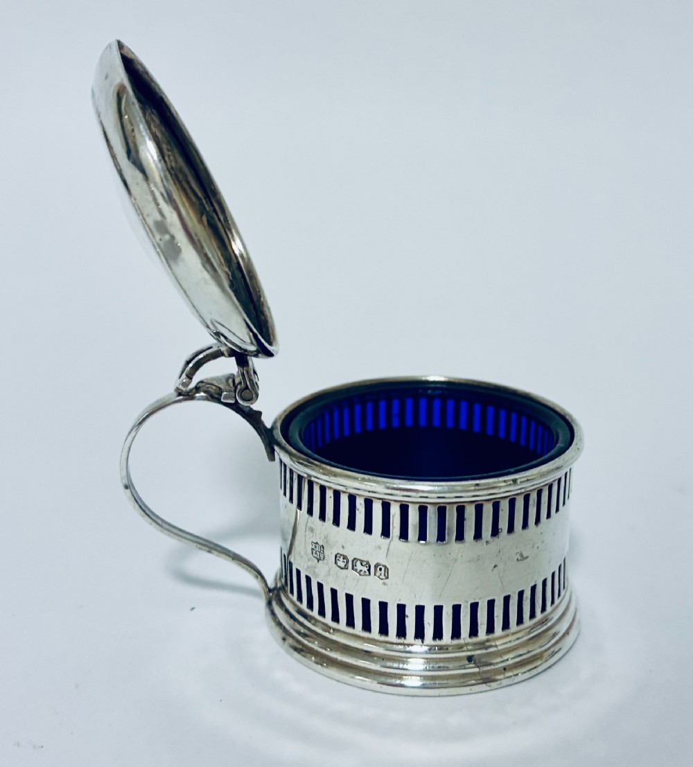 An antique three-piece silver cruet set featuring pierced vertical slot details, a mustard pot with lid and spoon, and two matching pepper casters. View XII