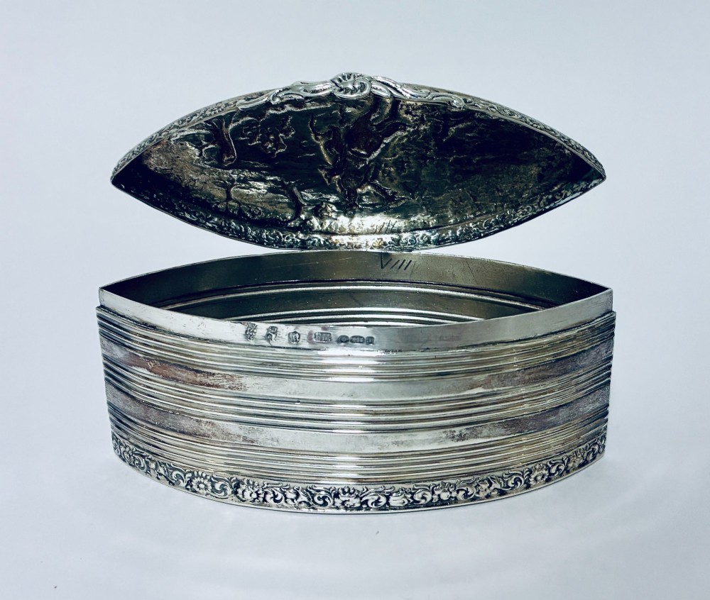 An oval silver snuff box featuring a relief equestrian scene on the hinged lid and reeded side walls with carved scroll borders. View III