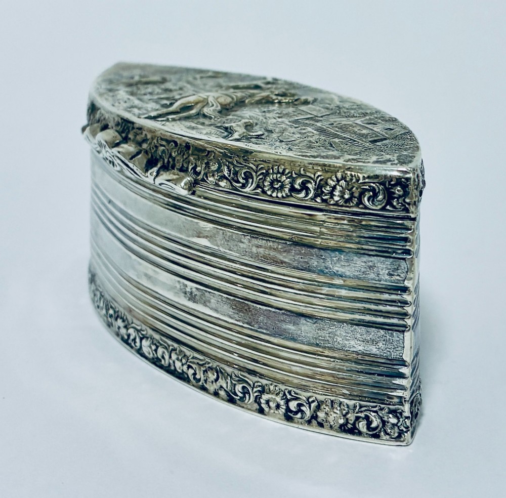 An oval silver snuff box featuring a relief equestrian scene on the hinged lid and reeded side walls with carved scroll borders. View V
