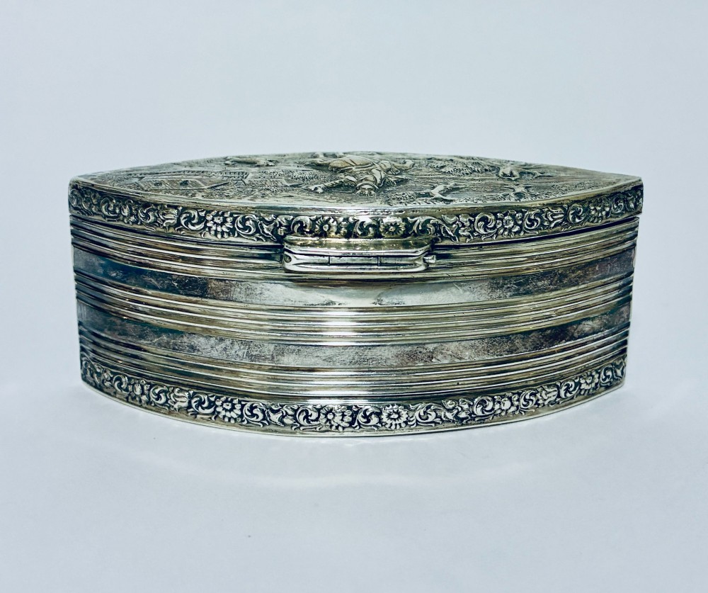 An oval silver snuff box featuring a relief equestrian scene on the hinged lid and reeded side walls with carved scroll borders. View VI
