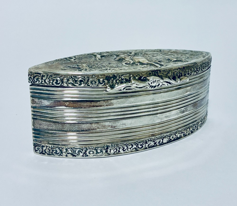 An oval silver snuff box featuring a relief equestrian scene on the hinged lid and reeded side walls with carved scroll borders. View VIII