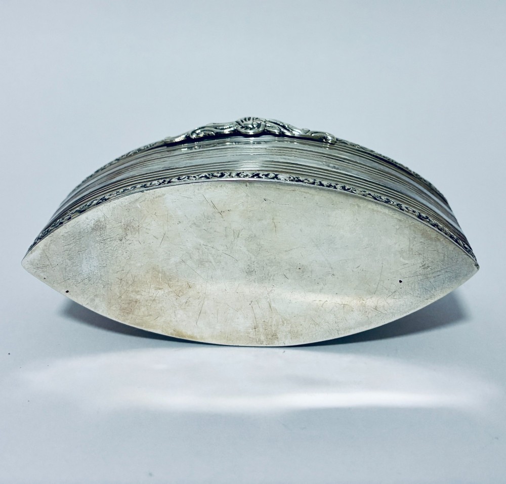 An oval silver snuff box featuring a relief equestrian scene on the hinged lid and reeded side walls with carved scroll borders. View IX