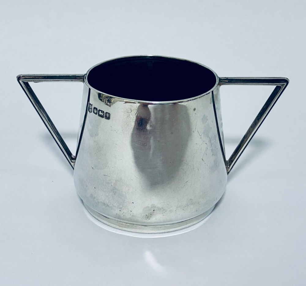 A polished sterling silver Art Deco sugar bowl with sharp triangular side handles and visible hallmarks stamped on the exterior wall.