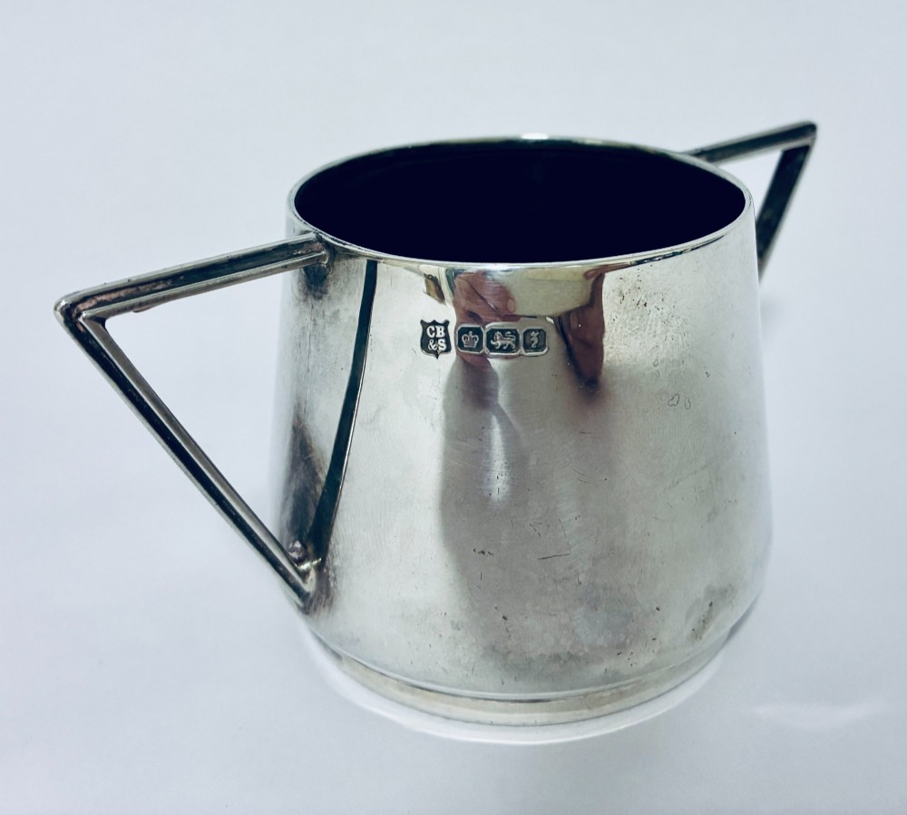 A polished sterling silver Art Deco sugar bowl with sharp triangular side handles and visible hallmarks stamped on the exterior wall. View II