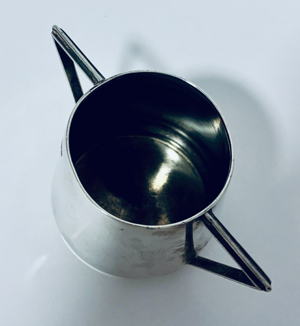 A polished sterling silver Art Deco sugar bowl with sharp triangular side handles and visible hallmarks stamped on the exterior wall. View VI