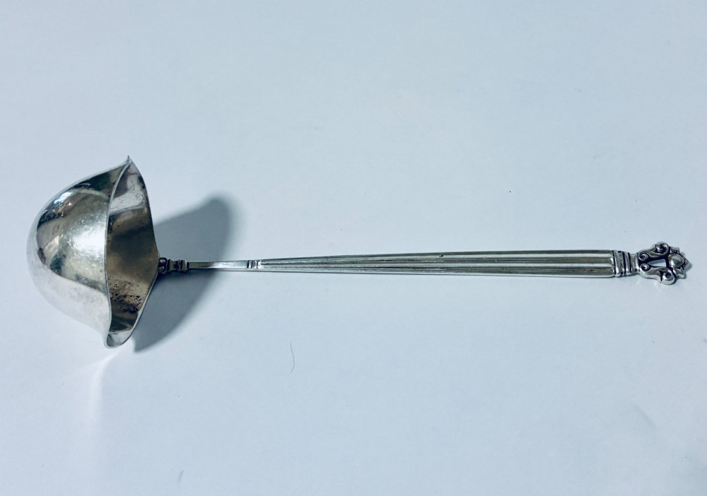 A sterling silver ladle featuring a deep bowl, a ribbed tapered handle, and a decorative scroll motif at the terminal.
