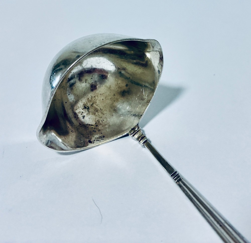 A sterling silver ladle featuring a deep bowl, a ribbed tapered handle, and a decorative scroll motif at the terminal. View III