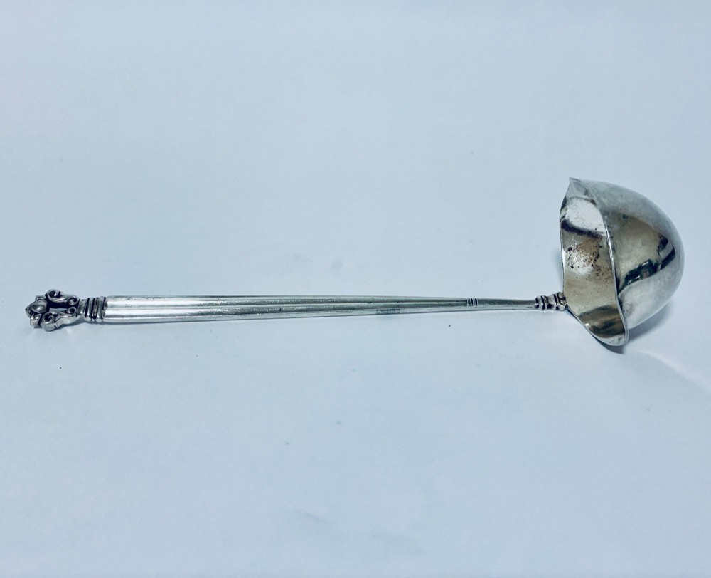 A sterling silver ladle featuring a deep bowl, a ribbed tapered handle, and a decorative scroll motif at the terminal. View VI