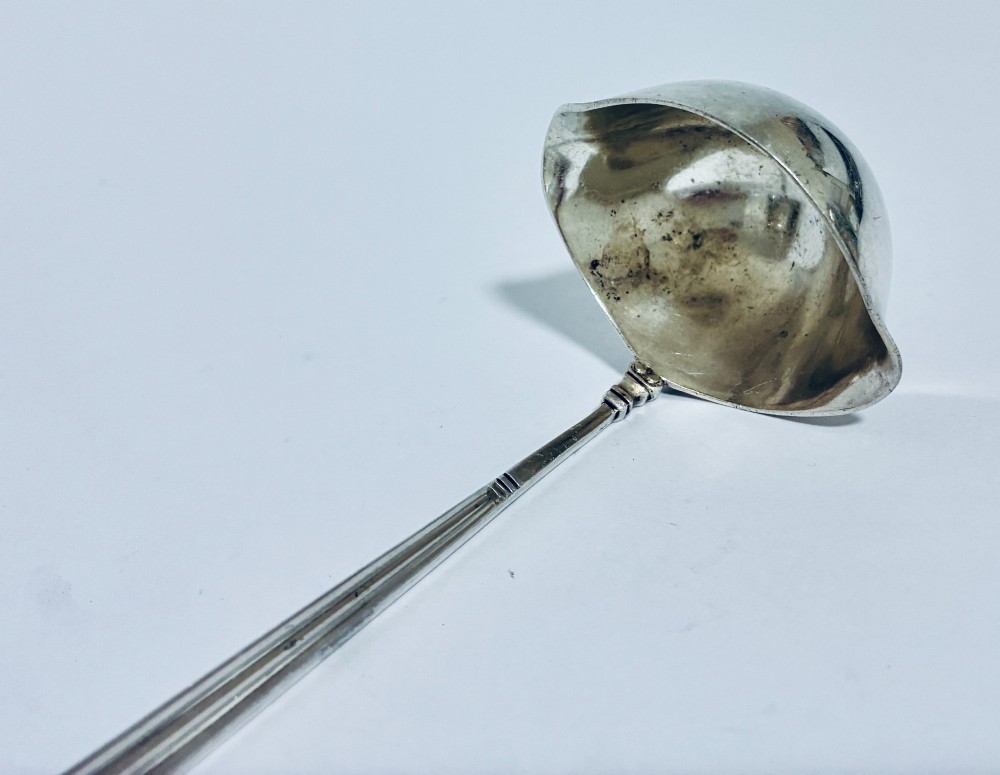 A sterling silver ladle featuring a deep bowl, a ribbed tapered handle, and a decorative scroll motif at the terminal. View VII