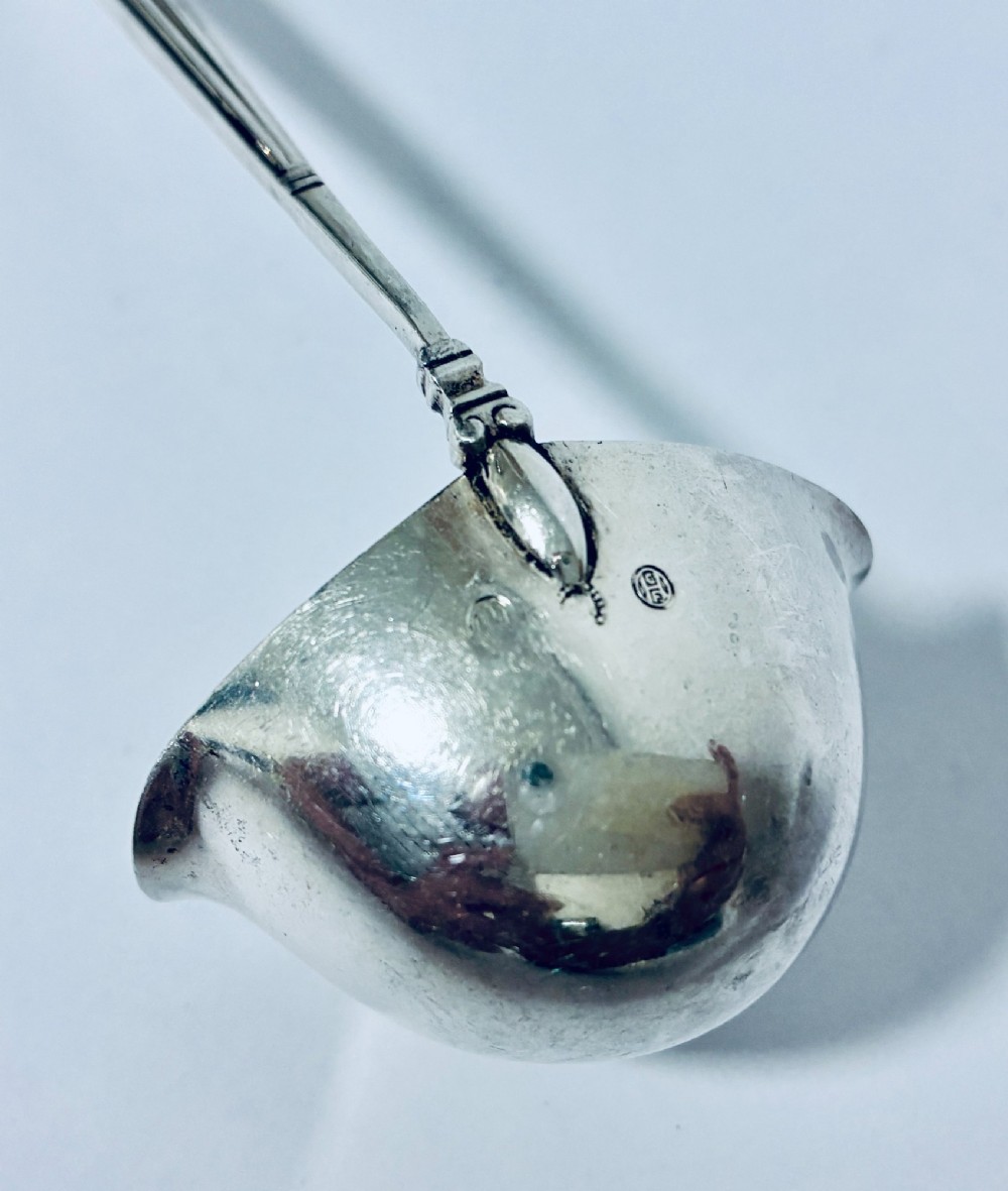 A sterling silver ladle featuring a deep bowl, a ribbed tapered handle, and a decorative scroll motif at the terminal. View X