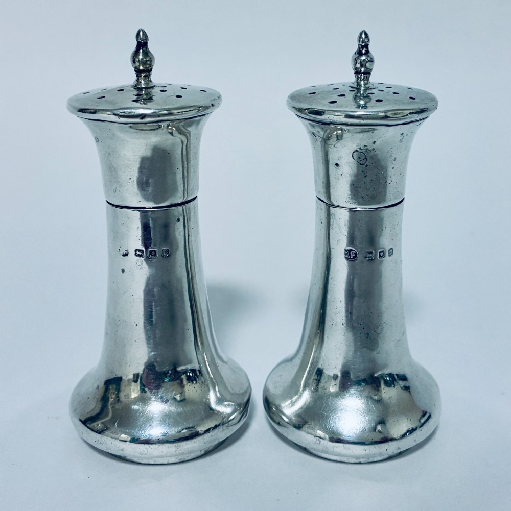 A pair of hallmarked sterling silver pepper pots featuring flared bodies, pierced tops, and turned finials.