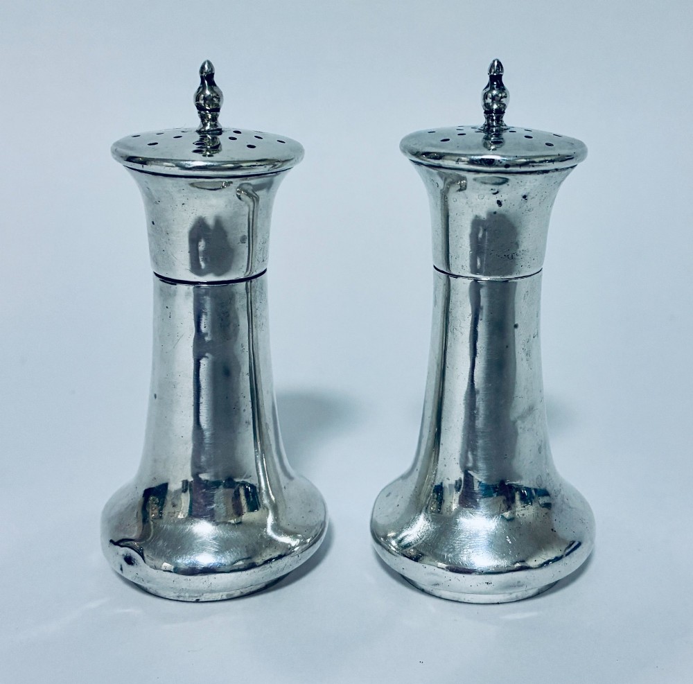 A pair of hallmarked sterling silver pepper pots featuring flared bodies, pierced tops, and turned finials. View V