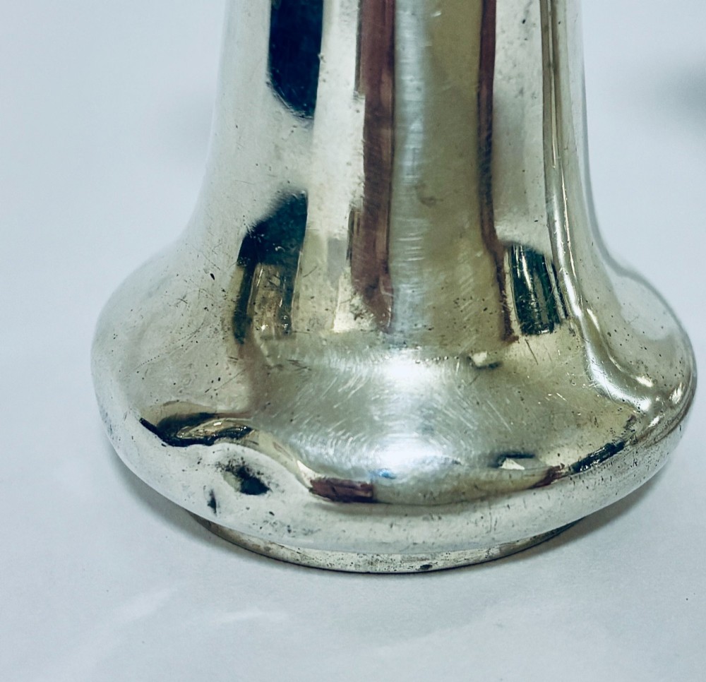 A pair of hallmarked sterling silver pepper pots featuring flared bodies, pierced tops, and turned finials. View VI