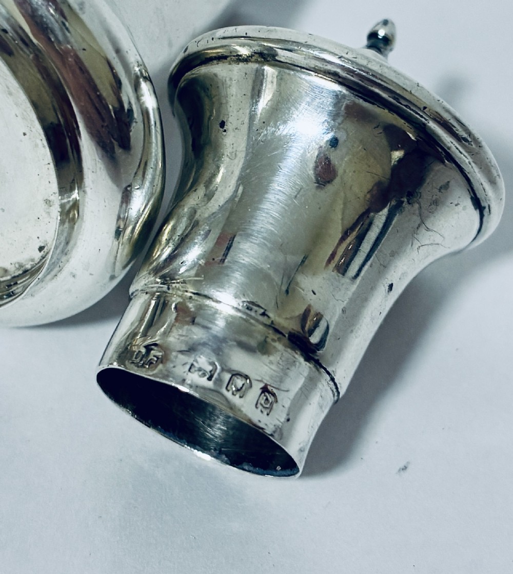 A pair of hallmarked sterling silver pepper pots featuring flared bodies, pierced tops, and turned finials. View X