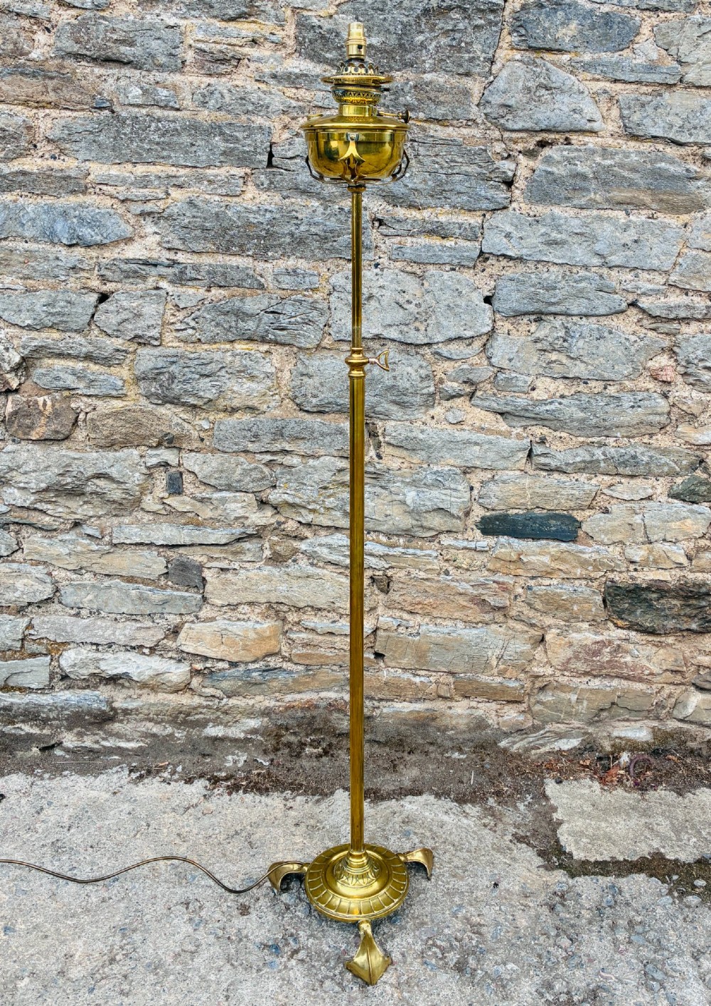 A Victorian brass telescopic floor lamp featuring a ornate tripod base, adjustable vertical stem, and converted oil font fitted with an electrical lamp holder.