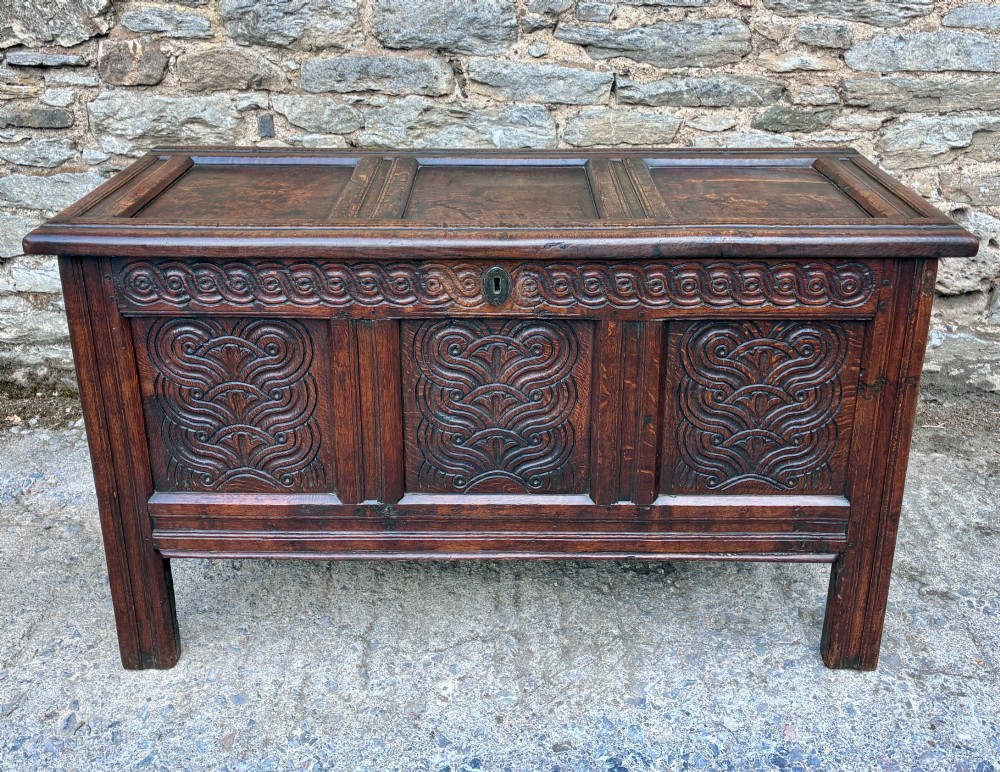 A dark oak 17th century coffer featuring a three-panel carved front with geometric scrollwork and a hinged rectangular lid.