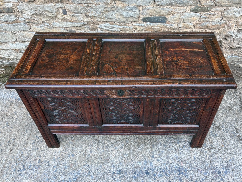 A dark oak 17th century coffer featuring a three-panel carved front with geometric scrollwork and a hinged rectangular lid. View II