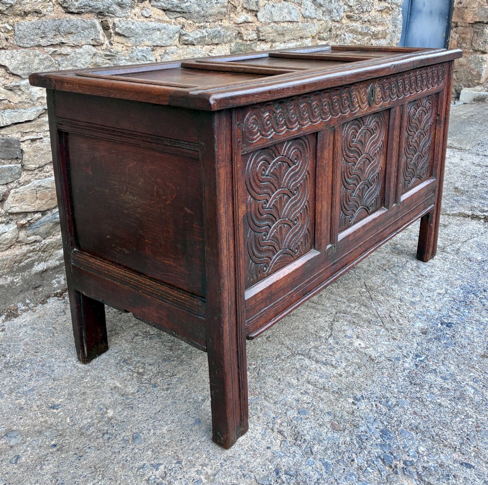 A dark oak 17th century coffer featuring a three-panel carved front with geometric scrollwork and a hinged rectangular lid. View III