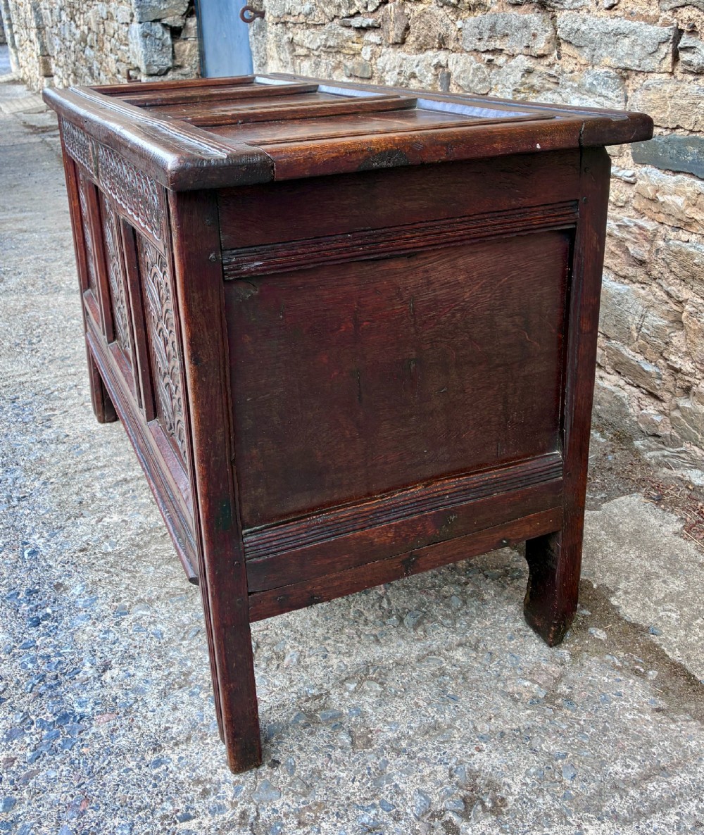A dark oak 17th century coffer featuring a three-panel carved front with geometric scrollwork and a hinged rectangular lid. View V