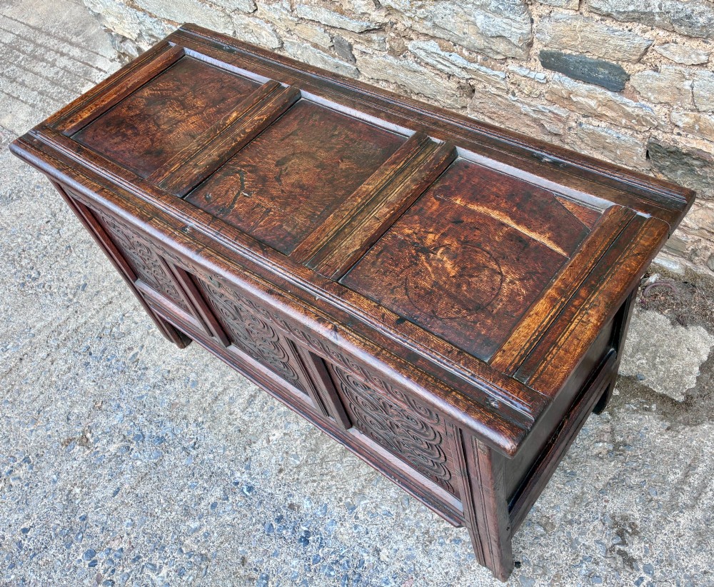 A dark oak 17th century coffer featuring a three-panel carved front with geometric scrollwork and a hinged rectangular lid. View VI