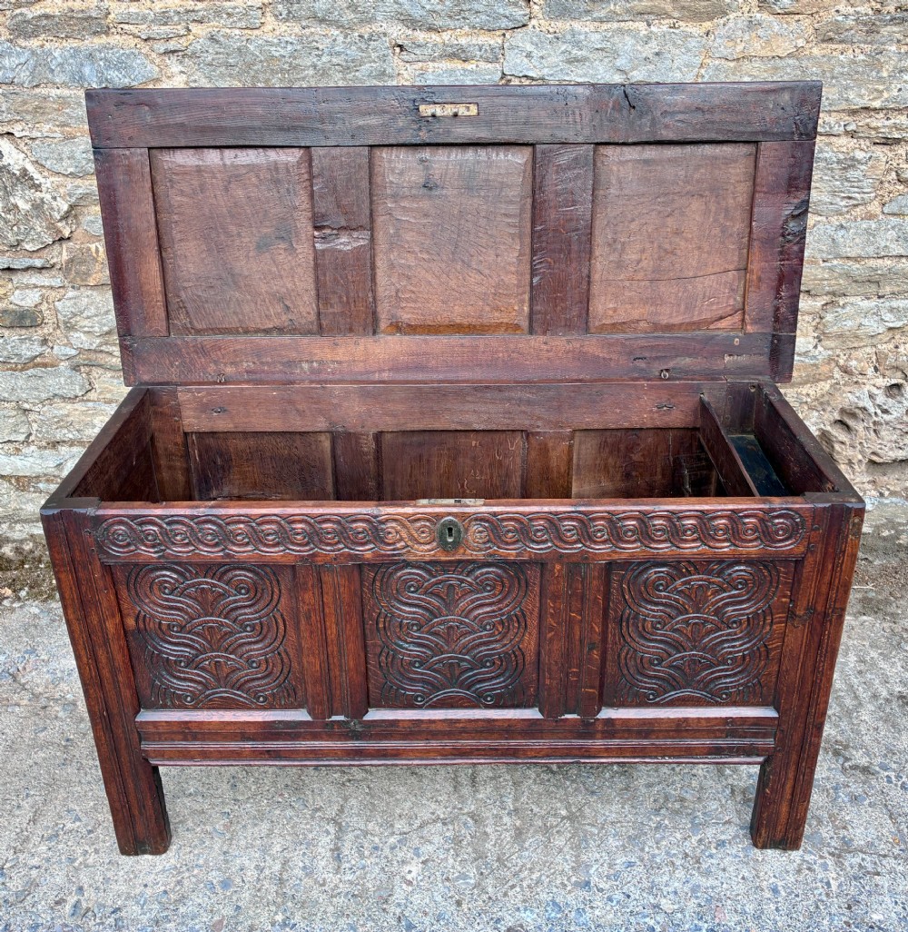 A dark oak 17th century coffer featuring a three-panel carved front with geometric scrollwork and a hinged rectangular lid. View VII
