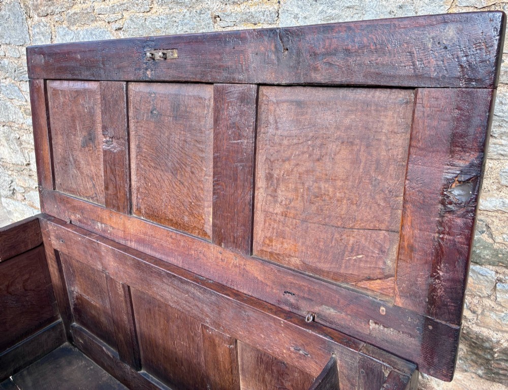 A dark oak 17th century coffer featuring a three-panel carved front with geometric scrollwork and a hinged rectangular lid. View X
