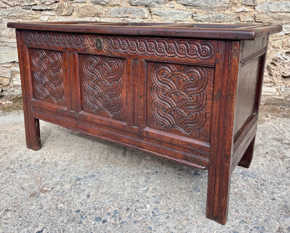 A dark oak 17th century coffer featuring a three-panel carved front with geometric scrollwork and a hinged rectangular lid. View XIII