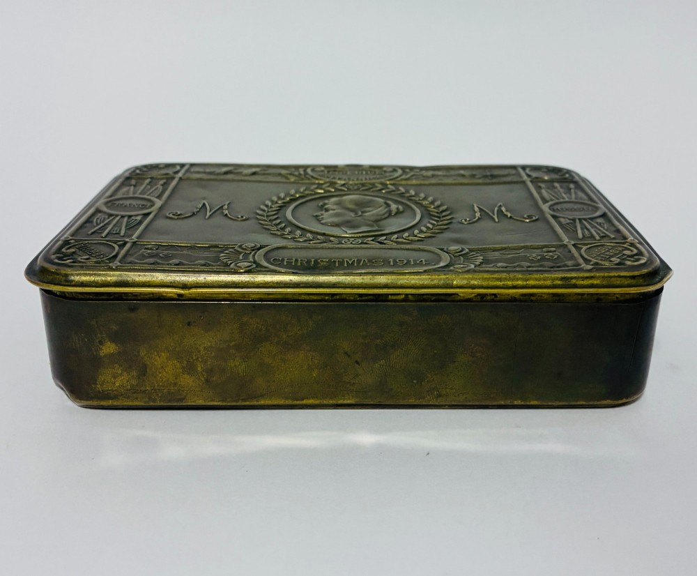 An embossed rectangular brass Princess Mary Christmas tin alongside its original cream greeting card printed with a red royal monogram. View III