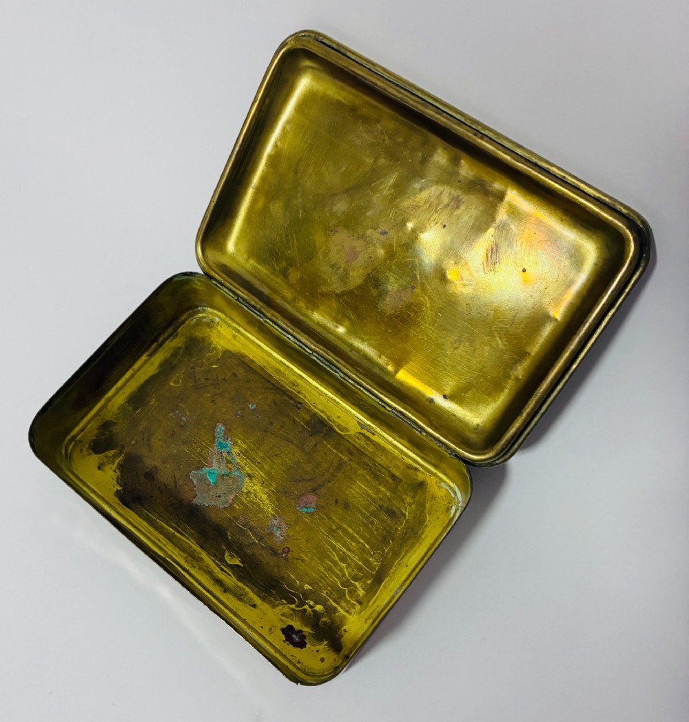 An embossed rectangular brass Princess Mary Christmas tin alongside its original cream greeting card printed with a red royal monogram. View IV